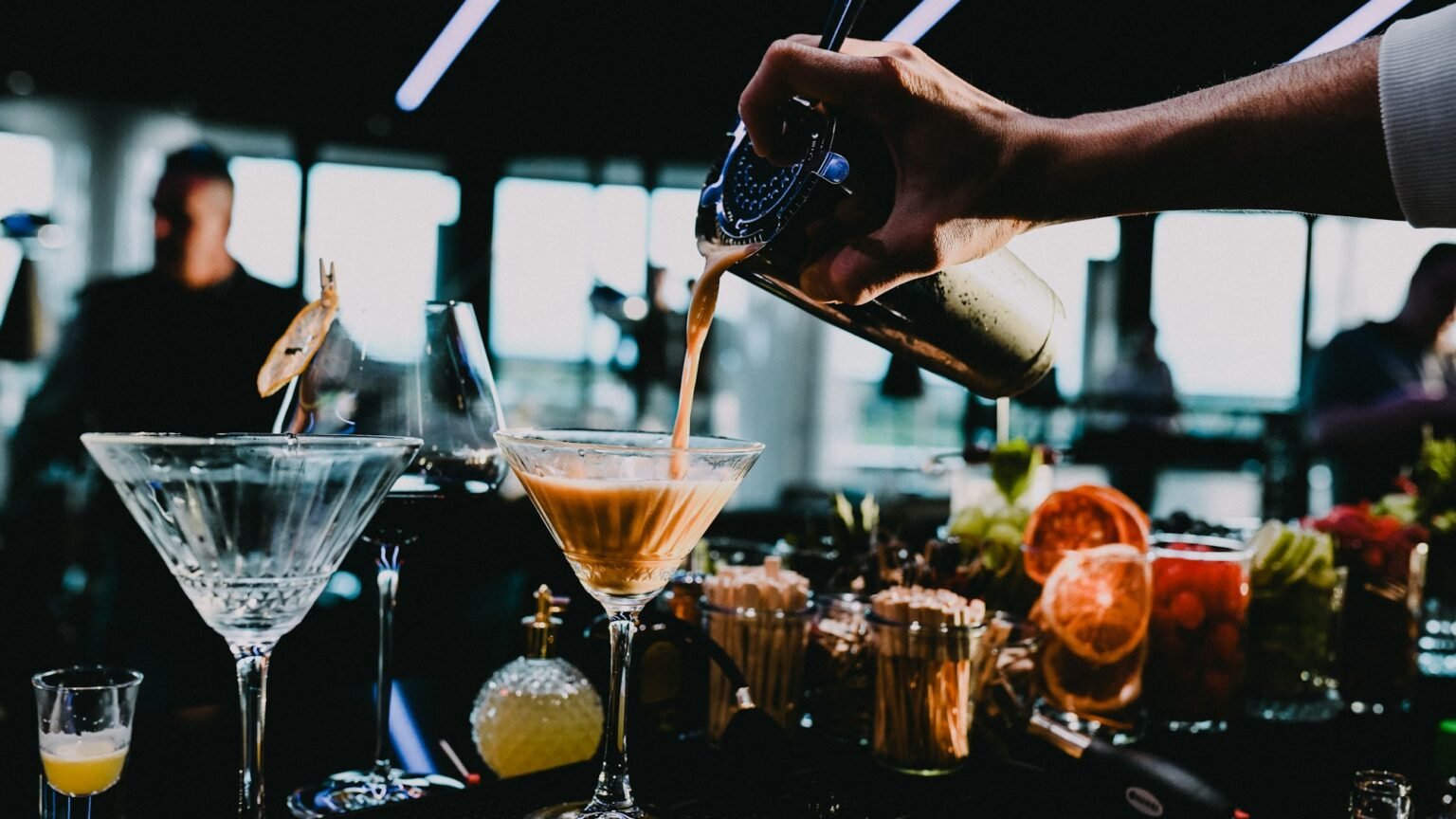 A bartender pouring a line of cocktails from a shaker