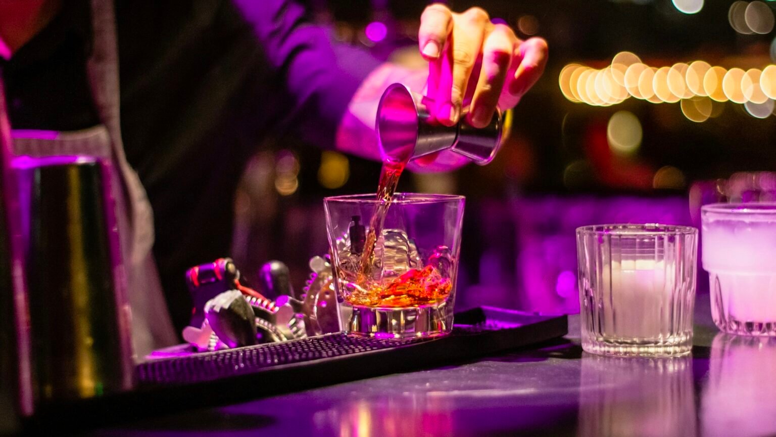 A bartender finishing a cocktail under purple light